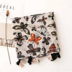 Détail d'une écharpe beige à imprimé papillon avec de délicats pompons noir et blanc