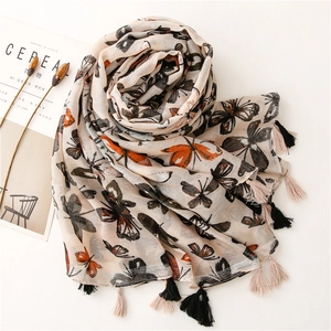 Écharpe beige à imprimé papillon avec pompons sur fond lifestyle avec un magazine