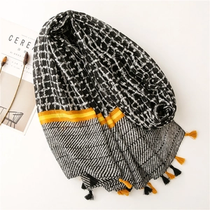 Detail of dark geometric grid scarf with vibrant yellow stripes and fringe tassels
