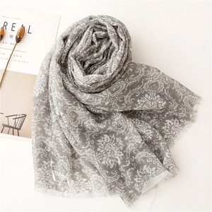 Detail of light gray floral print scarf with elegant white patterns and fringe edges