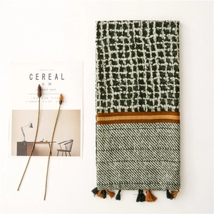 Detail of dark green geometric grid scarf with fringe tassels and soft linen texture