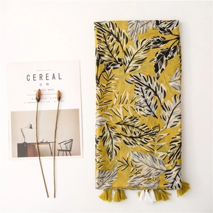 Longue écharpe jaune en coton avec imprimé feuilles tropicales et pompons sur fond blanc