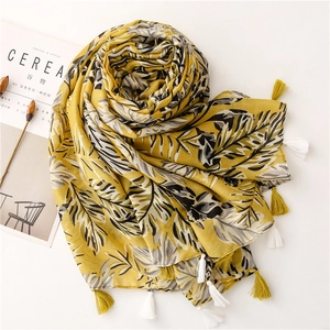 Détail d'une écharpe jaune à motif de feuilles de bananier avec pompons et coton doux