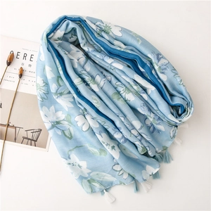 Dettaglio della sciarpa azzurra con stampe floreali bianche e decorazione con nappe