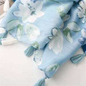 Dettaglio di una sciarpa azzurra con stampa floreale e nappe decorative ai bordi