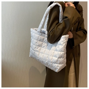 Detail of white quilted puffer tote bag on a model wearing a brown wool coat