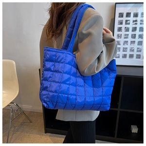 Quilted blue nylon tote bag with wide shoulder strap worn over a grey blazer jacket