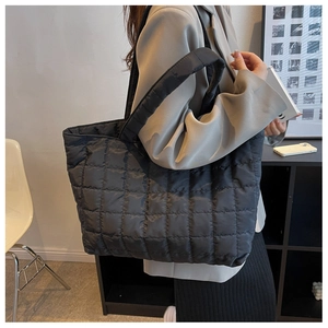 Close-up of black quilted down tote bag worn by model in a minimalist indoor setting