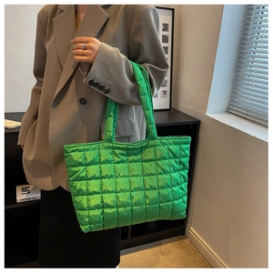Green quilted nylon tote bag worn by a model in a stylish indoor studio setting