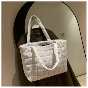 Detail of white quilted tote bag featuring a magnetic clasp and grid stitching texture