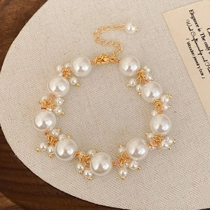 Elegant white pearl bracelet with gold lobster clasp and adjustable chain on a beige base