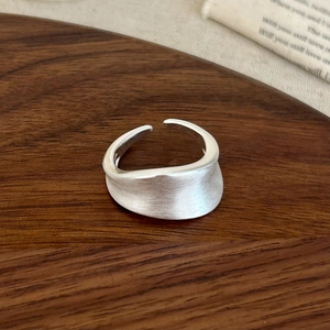Minimalist silver irregular brushed wavy open ring on a vintage wooden tray background