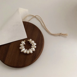 Elegant C-shaped ear cuff featuring waterdrop pearls with golden metal accents on wood