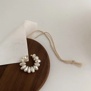 Detail of C-shaped pearl ear cuff with gold beads on a rustic wooden platter