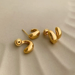 Puces d'oreilles dorées minimalistes aux courbes organiques sur une surface beige