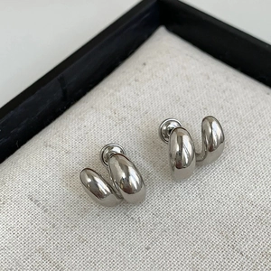 Gros plan de boucles d'oreilles doubles anneaux argentés sur tissu texturé blanc