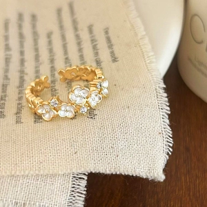 Golden open ring with white enamel flowers and zircons on a rustic cloth background