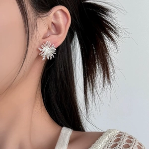 Close-up of a silver fireworks-shaped zircon stud earring on a female model's ear