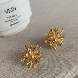 Detailed shot of gold firework starburst earrings with white zircon on grey surface