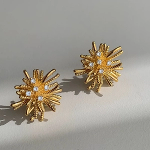 Detailed view of gold firework stud earrings with sparkling cubic zirconia on grey background