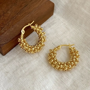 Detail of gold beaded hoop earrings featuring a textured ball surface on wooden display