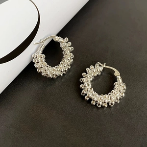 Macro detail of silver bead-textured hoop earrings with a dense metallic woven pattern
