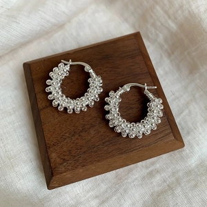Detailed close-up of silver beaded hoop earrings on a dark wood and fabric background