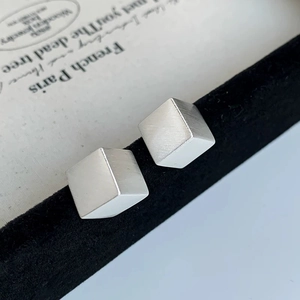 Macro shot of silver cube stud earrings featuring a brushed matte metallic texture