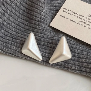 Macro detail of geometric triangular stud earrings with matte brushed silver finish