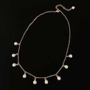 Collana dorata con nove perle bianche e chiusura regolabile su sfondo nero elegante