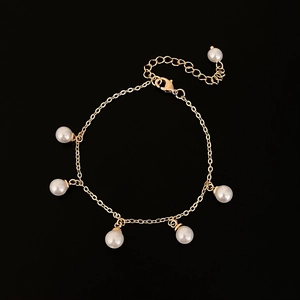 Dettaglio di un bracciale dorato con nappe di perle bianche e catena a maglie classiche