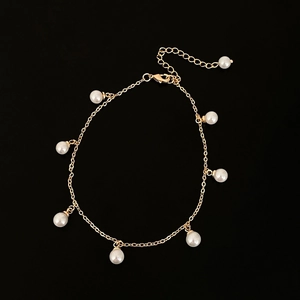Dettaglio di un bracciale a catena dorata con diverse perle finte bianche pendenti