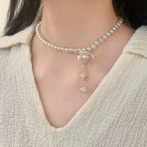 Collier de perles de style français avec fleur blanche et pampille dorée porté par un modèle