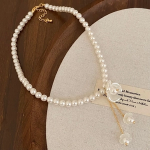 Détail d'un collier de perles à fleurs avec pampilles dorées et pendentif blanc