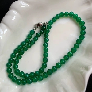 Macro view of green chalcedony beaded necklace with silver clasp on white shell tray