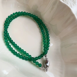 Close-up of elegant green chalcedony beaded necklace with a silver oval clasp on a ceramic tray