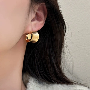 Elegant gold-plated wide C-shape brushed metal earrings worn by a model in a side view