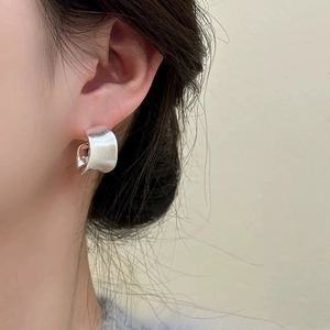 Close-up of minimalist brushed silver stud earring featuring wide geometric silhouette