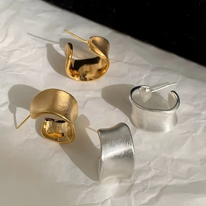 Detailed macro of irregular C-shaped brushed metal earrings in gold and silver finish
