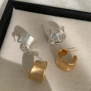 Detail of irregular C-shaped wave earrings in brushed gold and silver finish