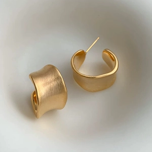 Detail of matte gold irregular wave earrings with brushed texture and modern geometric style
