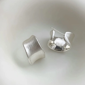 Close-up of C-shaped earrings with brushed silver texture and polished inner finish