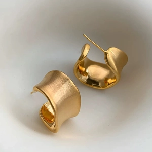 Macro detail of gold irregular C-shape earrings with brushed finish and polished inner surface