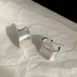 Macro shot of minimalist silver stud earrings with brushed matte texture and C-shape design