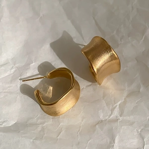 Macro detail of gold brushed C-shaped earrings with matte metallic texture and side lighting