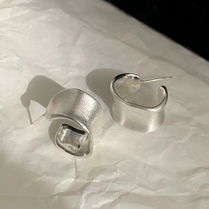 Detailed view of brushed silver irregular C-shape earrings on white textured background
