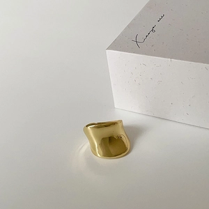 Detailed shot of a minimalist gold wide ring with irregular wave design on a white prop box