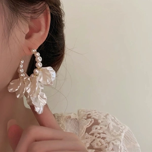 Grandes créoles dorées élégantes avec perles blanches et pétales sur un mannequin