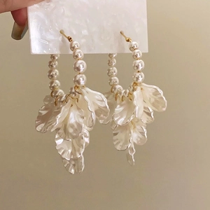 Détail de boucles d'oreilles créoles avec perles et pétales de fleurs blanches en résine