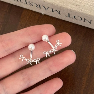 Gros plan de boucles d'oreilles nœud argentées avec perle blanche tenues à la main